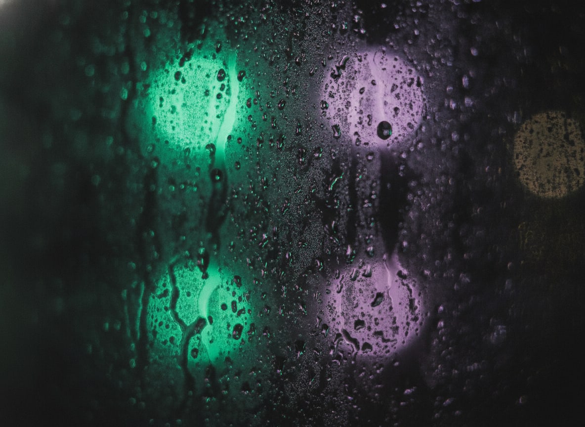 Abstract macro of condensation and fine water droplets on a dark window pane at night, soft out-of-focus green and viole